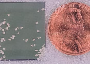 Silicon chip that integrates both imaging sensors and data compression, shown next to a U.S. penny and resting on grains of sand.