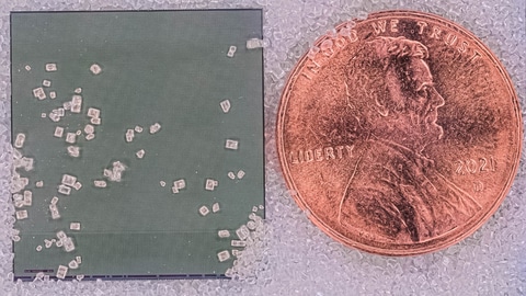 Silicon chip that integrates both imaging sensors and data compression, shown next to a U.S. penny and resting on grains of sand.